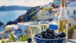 Greek aniseed drink Ouzo in a glass bottle with two shot glasses and Greek olives on a traditional ceramic dish, with a landscape of the Mediterranean coastline in the background.