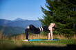 Woman practicing yoga outdoors in the mountains in a serene, natural setting. Female performing yoga pose on mat, with backdrop of beautiful mountain landscape at sunrise or sunset.