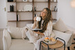 © polinaloves - Young woman reading book and drinking tea, sitting on sofa in a cozy living room.