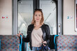 Young blond woman in jeans, shirt and leather jacket holding her smart phone and purse while riding modern speed train arriving to final train station stop. Travel and transportation