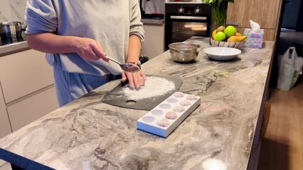 Wall Mural - A woman is making cookies on a marble countertop. She is using a spatula to mix the dough