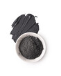 Cosmetic black clay powder in white ceramic bowl with a smear