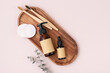 Brown glass cosmetic bottle, bamboo toothbrushes and cotton pads on a wooden tray.