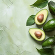Sliced and whole avocados with leaves lying on a green table. Top view. Food background with copy space.