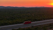 AERIAL: A red bus travels down the highway under a captivating crimson sunset.