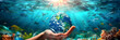 © Planetz - underwater view of a hand holding the Earth, with plastic bottles floating in water below  as pollution continues to increase	and sunlight shining on it. sea pollution