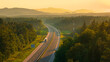 AERIAL: Trucks and cars travel along the scenic highway in golden evening light. Asphalt motorway winds through the beautiful wooded and hilly countryside, bathed in the rays of setting summer sun.