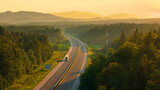 Fototapeta  - AERIAL: Trucks and cars travel along the scenic highway in golden evening light. Asphalt motorway winds through the beautiful wooded and hilly countryside, bathed in the rays of setting summer sun.