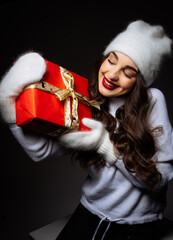 Wall Mural - A woman is holding a red box with a gold ribbon on it. She is wearing a white hat and a red lipstick.