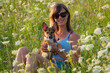 PORTRAIT, DOF: A smiling woman in sunglasses embraces her adorable young puppy as they pose in the middle of a vibrant meadow of blooming wildflowers. Moments of happiness with a cute furry companion.