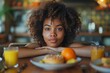Curly-haired woman sitting at a table with breakfast items, looking directly at the camera