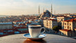 Traditional Turkish coffee in porcelain mug on table in front of blurry Istanbul view with buildings, bridge and a mosque during sunset.