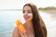 Beautiful Young woman with sun cream on face. Girl holding sunscreen bottle on the beach and applying moisturizing lotion on skin.Skin care. Sun protection. Suntan