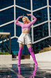 Stylish Woman In Pink Crop Top And White Skirt Poses Dramatically With Pink Boots Against A Modern Glass Building. Perfect For Fashion And Lifestyle Themes. Vertical Screen. Ideal For Social Media.