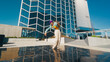 A Vibrant Young Woman Dances Energetically In Front Of A Modern Glass Building, Showcasing A Blend Of Urban Architecture And Youthful Exuberance Under A Clear Blue Sky.