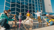 Vibrant Outdoor Scene Of Diverse Young Adults Energetically Dancing In Front Of A Modern Glass Building, Showcasing Friendship And Cultural Expression Through Dynamic Movements And Casual Urban Wear.