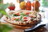 Fototapeta Tulipany - Wood fired Italian pizza with prosciutto, parma ham, arugula, and parmesan, on a wooden cutting board, selective focus.