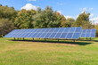 Rows of solar panels on grass with trees in background on a clear autumn day