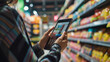 © Armin - Close-up of woman using tablet to compare grocery prices in a well-stocked supermarket aisle