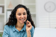 Cheerful Hispanic woman using a headset during a remote working session. She appears engaged and happy, sitting at her home office desk.