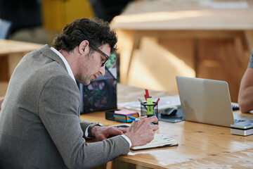 Canvas Print - Businessman, notebook and brainstorming at desk for project, planning and teamwork in office. Mature male person, collaboration and research in workplace for start up company and global enterprise