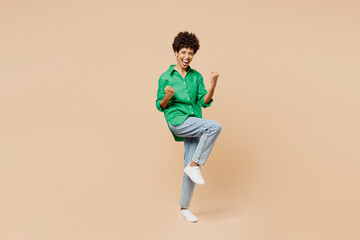 Wall Mural - Full body young woman of African American ethnicity wear green shirt casual clothes doing winner gesture celebrate clenching fists isolated on plain pastel light beige background. Lifestyle concept.