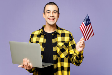 Wall Mural - Young student IT middle eastern man wears yellow shirt casual clothes hold American flag use work on laptop pc computer isolated on plain pastel purple background studio portrait. Lifestyle concept.