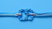   A Tight Shot Of A Blue Zipper, Scissors Positioned In Its Center Against A Blue Background