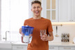 Happy man with filter jug and glass of clear water in kitchen