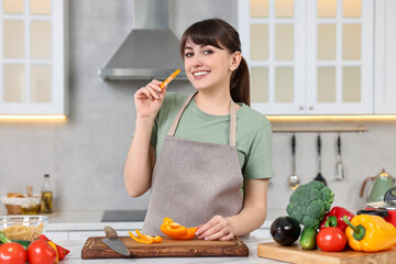 Happy young housewife with cut bell pepper cooking at white marble table in kitchen