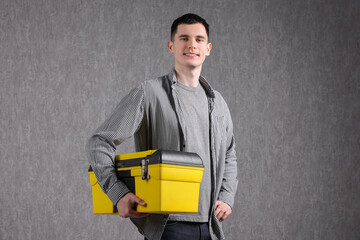 Wall Mural - Young man with tool box on grey background