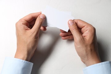 Canvas Print - Man holding blank cards at white table, top view. Mockup for design