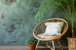 Rattan chair with decorative cushion and opened notebook with empty pages next to potted plant against green wall in bohemian style living room. Cozy place to sit in apartment