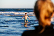 Boy have fun on the sea waves while mother watching him carefully in a sunset of a sunny summer day.