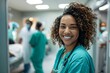 © dreamdes - Cheerful female nurse smiling in busy hospital. African american woman. Beautiful medical worker in scrubs. Medicine and healthcare concept.
