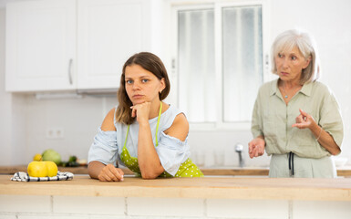 Wall Mural - Offended young woman listening her senior mother standing behind and quarreling with her.