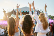© artiemedvedev - Group of female friends enjoying live music on sunny beach festival. Girls dance, celebrate with hands up in summer vibe. Casual fun, youth culture, outdoor event by sea. Friendship, lifestyle moment.