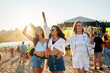 © artiemedvedev - Group of happy young women dance at a beach festival, sunset lights their carefree moves. Friends in summer attire enjoy music, sandy shores, sea breeze. Casual outdoor event, youth culture, freedom.