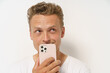 A man is holding a phone and looking at it. He has a smile on his face. The phone is pink and has a white case