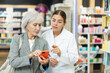 Female pharmacist and elderly woman customer reading prescription together on smartphone screen in pharmacy