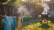 A person hanging clothes on a line in the backyard while a grill smokes in the background, hinting at a summer cookout.
