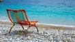 A colorful woven beach chair on a pebbled Mediterranean beach with turquoise water in the background.
