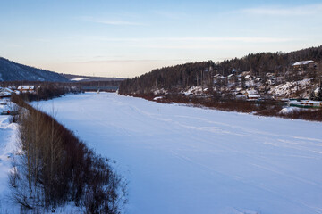 Wall Mural - View of the Tynda River and the outskirts of the city of Tynda, Amur Region, Russia. Winter landscape. Frozen river. The ice is covered with snow. Houses on the shore and on the slope of the hill.