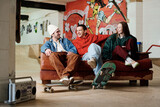 Fototapeta  - Group of three modern male and female friends hanging out in skatepark sitting on couch, chatting and listening to music, copy space