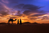 Fototapeta  - Silhouette of camel and man in arabian dress with woman against sunset sky background, beautiful desert landscape