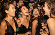 © Kien - A photo of a group of people at an elegant party, with confetti flying around and smiling women in black dresses standing next to men wearing tuxedos who are laughing