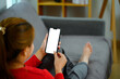 Cropped shot casual young woman sitting on sofa holding mobile phone with blank screen