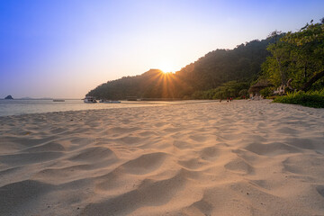 Golden hour sunlight bathes a secluded beach, highlighting the textured sand and tranquil scenery