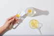 The woman's hand is holding a test tube on a white background along with other glassware containing calendula petals. Minimalist scene featuring an advertisement for cosmetics with calendula extract