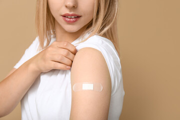 Canvas Print - Young woman with medical patch on arm against beige background, closeup. Vaccination concept